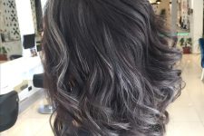 medium-length volumetric dark hair with grey highlights and waves looks very chic and bold and brings a natural look