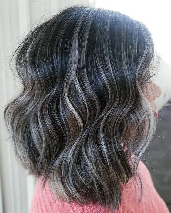 Medium length wavy black hair with silver balayage that helps naturally grey hair blend in