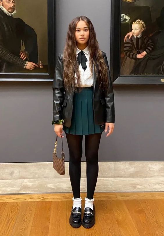 a lovely preppy look with a white shirt, a dark green pleated mini, black tights, white socks, black shoes and a black leather jacket