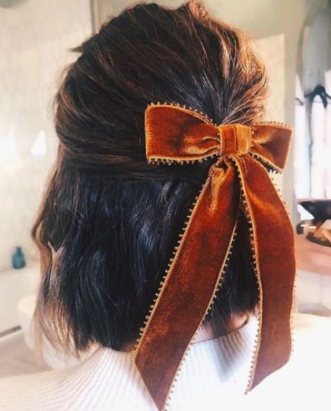 A long bob styled as a half updo with a rust colored velvet bow is a stylish idea for Christmas