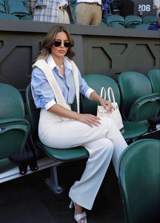 a classic and elegant old money look with a blue shirt, a white pullover, white high-waisted pants, heels and a bag