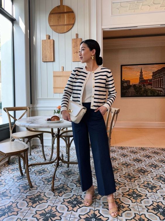 a classic old money outfit with a white t-shirt, a striped cardigan, navy pants, tan shoes and a small white bag