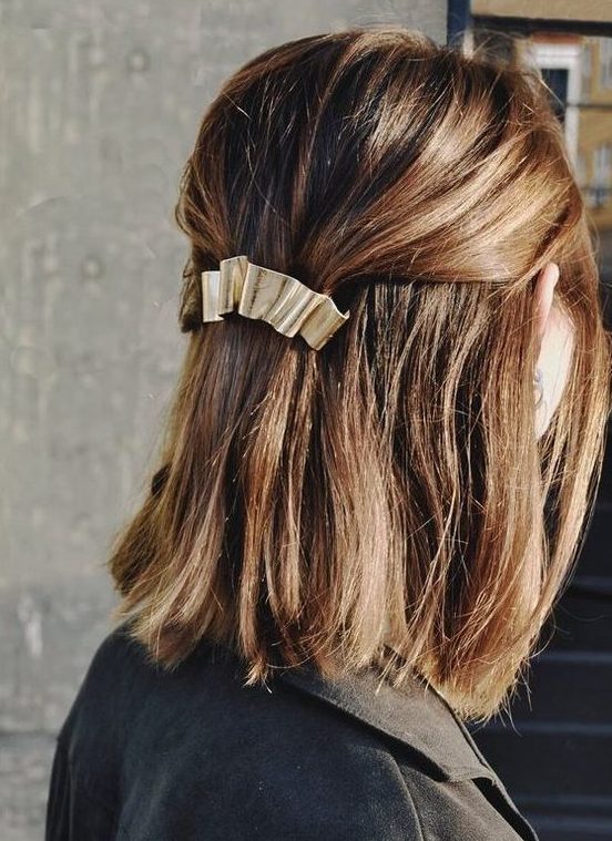 a classy half updo with a bump on top and straight hair down and a metallic hair barrette for a modern holiday party look