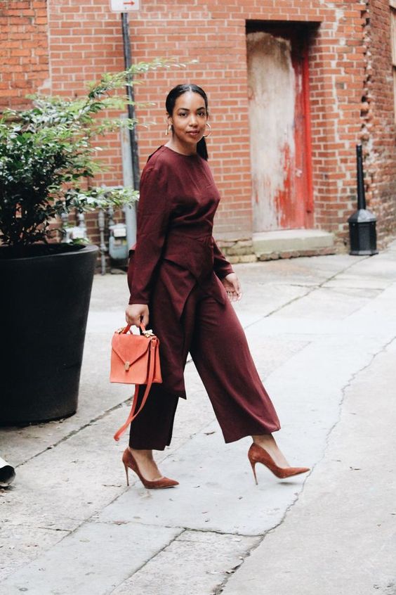 a burgundy jumpsuit with a catchy waist detail, brown shoes and an orange bag for a fall work look