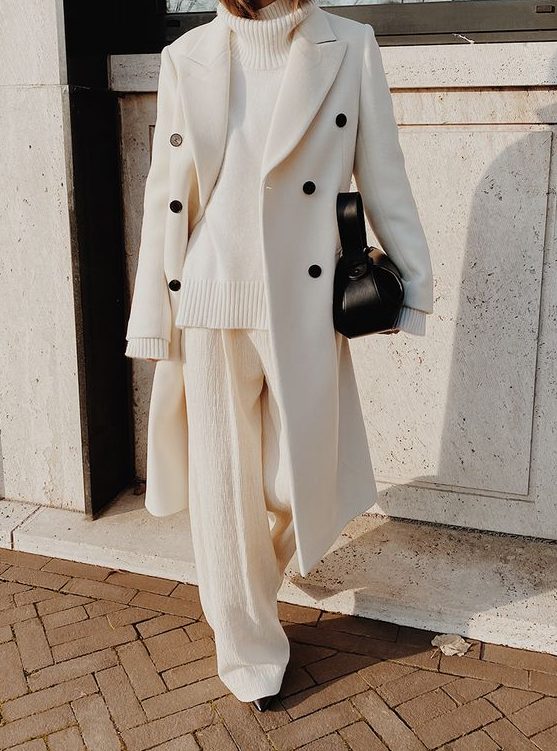 a white sweater, white pants, a white coat with black buttons and a black bag plus black booties