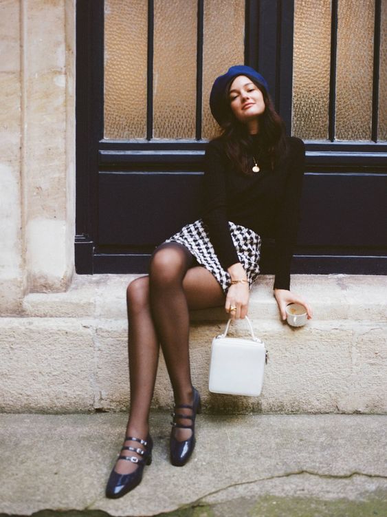 a Parisian chic look with a black top, a printed mini skirt, black tights, black Mary Jane shoes and a white bag plus a beret