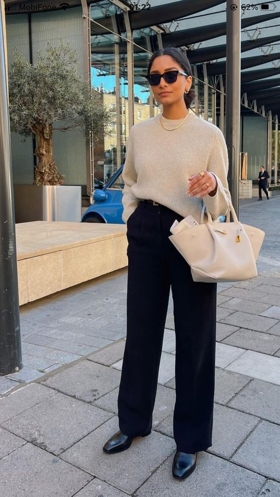 a beautiful quiet luxury look with a neutral oversized jumper, black pants, black shoes and a white bag plus a chain necklace