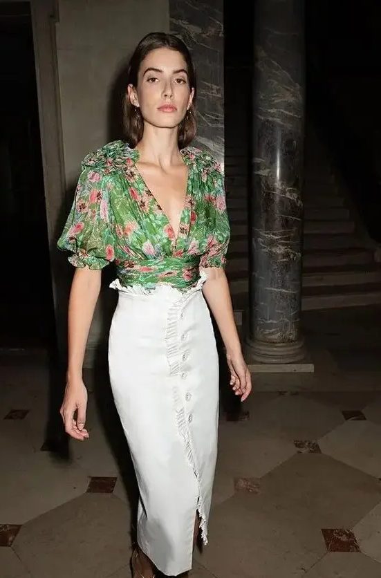 a beautiful wedding guest look with a green floral blouse with a deep V-neckline and a white ruffle skirt with a row of buttons