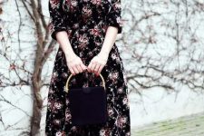 a black midi floral dress with short sleeves, black heels and a black bag with a gold handle