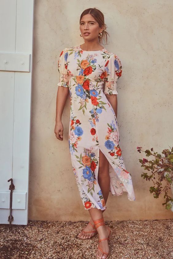 a bold spring wedding guest look with a colorful floral dress with a slit, orange lace up shoes and gold earrings