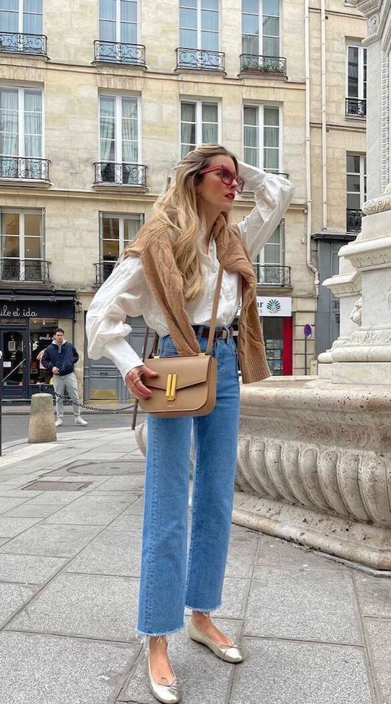 a casual outfit with a white blouse, blue jeans, silver flats, a beige jumper and a beige bag
