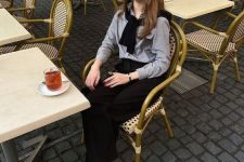 a classy old money outfit with a grey shirt, a black pullover, black wideleg pants, black slingbacks