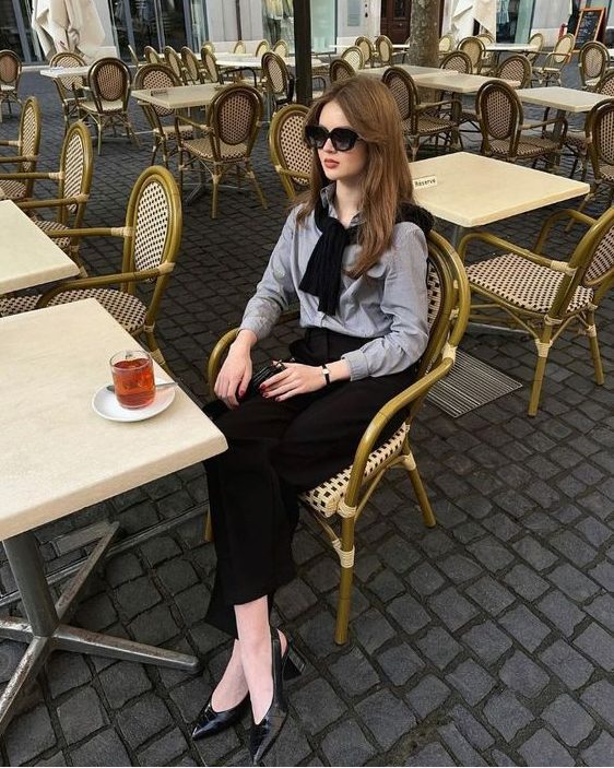 a classy old money outfit with a grey shirt, a black pullover, black wideleg pants, black slingbacks