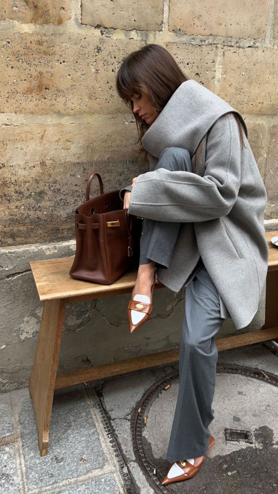 a cool winter quiet luxury look with a grey pantsuit, a grey oversized coat, brown heels, a brown tote and a large scaef