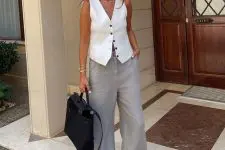 a cool work old money look with a white waistcoat, grey wideleg pants, white slippers and a black bag plus layered necklaces