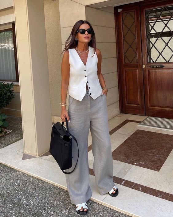 a cool work old money look with a white waistcoat, grey wideleg pants, white slippers and a black bag plus layered necklaces