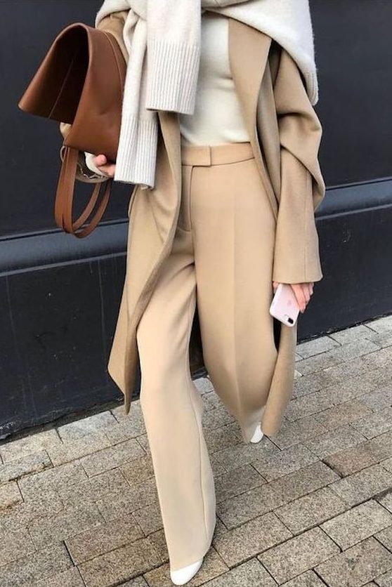 a creamy turtleneck, beige pants and a coat, a neutral sweater over the shoulders, creamy boots and a brown bag