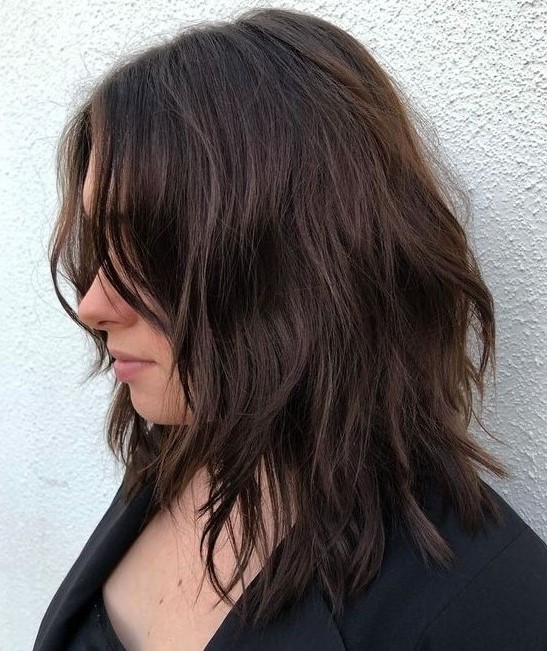 a dark brown choppy medium haircut with side bangs and messy waves shows off some texture and dimension