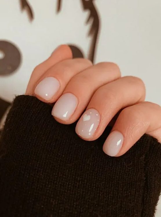 a delicate nude manicure with milky and blush nails and a heart plus polkd dots on the ring finger is amazing for a cute look