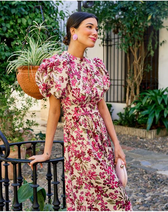 a fun wedding guest look with a bright floral dress with puff sleeves, pink earrings and a pink clutch is cool