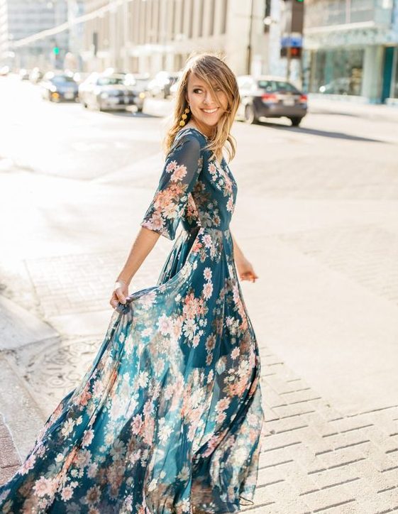 a flowy dark green maxi dress with a pink floral print, long sleeves and statement earrings