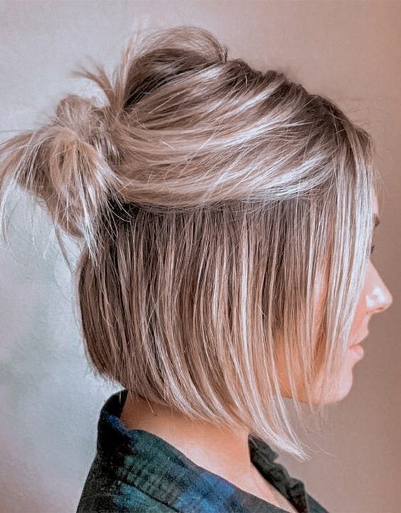 A long bob styled as a half updo with a messy bump and a small knot plus face framing hair
