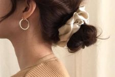 a low bun with twisted hair and face-framing bangs plus a scrunchie is a cool hairstyle for Christmas