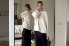 a minimalist quiet luxury outfit with a white oversized jumper, a black slip maxi skirt with a slit, brown loafers and a black bag
