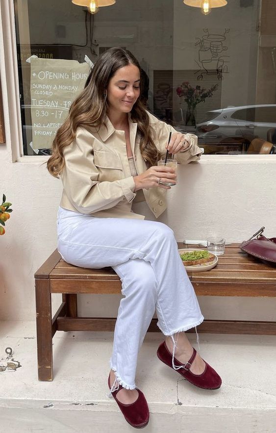 a neutral outfit with a tan top, a tan cropped jacket, white jeans and burgundy Mary Jane shoes