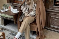 a preppy meets old money look with a white shirt, a greige waistcoat, beige pants, white socks, brown loafers and a brown coat