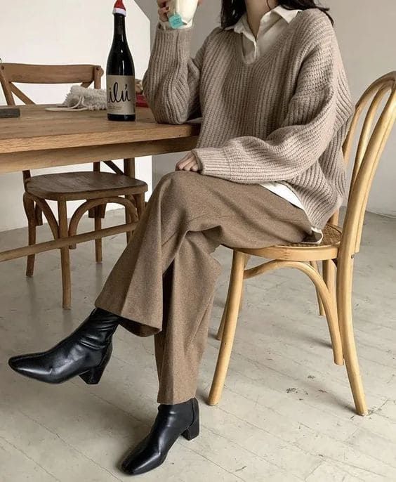 a quiet luxury look with an oversized shirt, a greige jumper, brown trousers, black boots is simple and cool