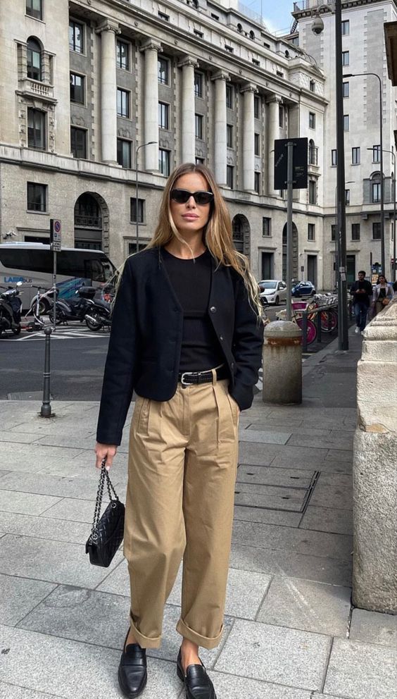A quiet luxury outfit with a black t shirt, a black cropped cardigan, beige high waisted trousers, black shoes and a black bag