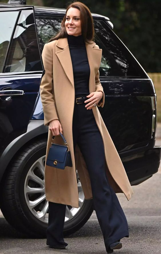 a quiet luxury outfit with a black turtleneck, flare trousers, black shoes, a camel midi coat and a small navy bag