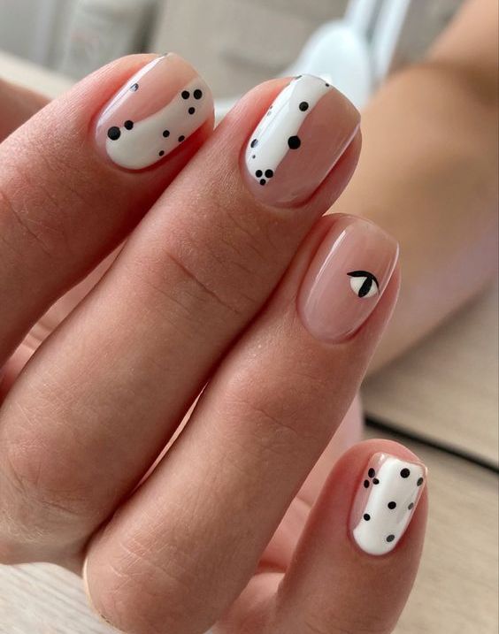 a quirky design on short square nails, nude nails with white patterns, speckles and an eye is cool