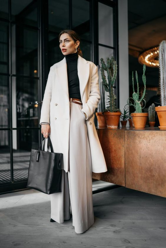 a refined quiet luxury work look with neutral palazzo pants, a black turtleneck, a creamy midi coat, black shoes and a black tote