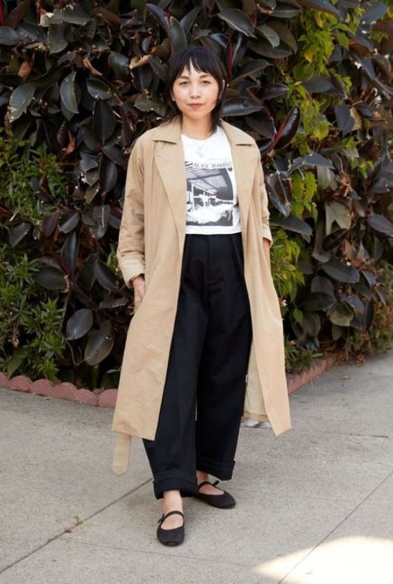 a relaxed outfit with a printed t-shirt, black baggy jeans, a tan trench and black Mary Jane shoes for spring