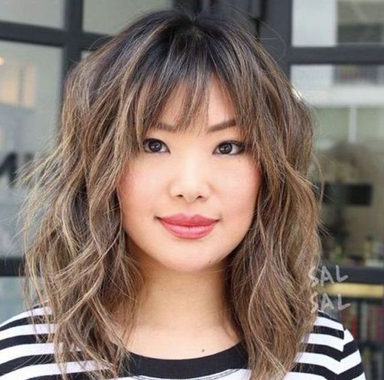 a shaggy long bob with caramel highlights and wispy and bottleneck bangs looks super cute and chic