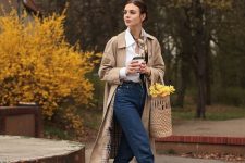 a spring or fall outfit with a white button down, navy jeans, black Mary Jane shoes, a tan trench and a basket