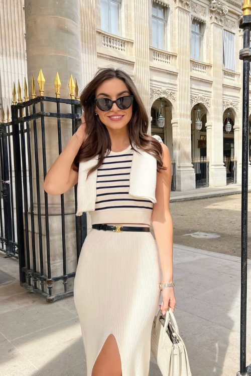 a striped sleeveless top, a creamy midi skirt with a thin black belt, a jumper over the shoulders and a creamy bag