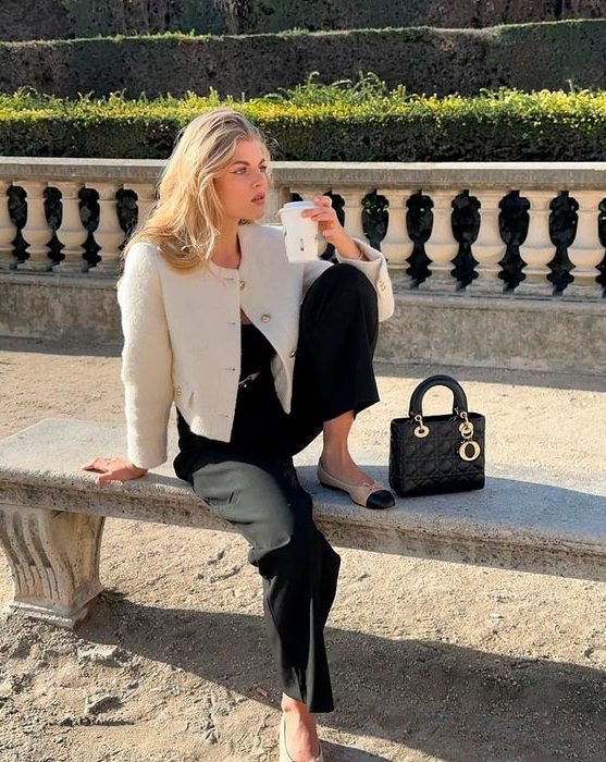 A stylish old money outfit with a black top, pants, a white cropped blazer, two tone flats and a black bag