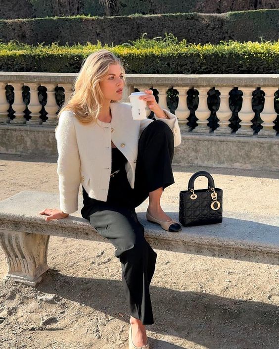 A stylish old money outfit with a black top, pants, a white cropped blazer, two tone flats and a black bag