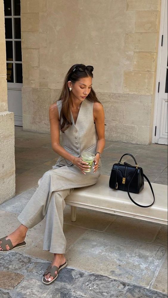 a summer work outfit with a grey waistcoat and trousers, grey slippers and a black bag is timeless and cool