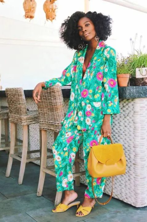 a super bright floral print pantsuit with an oversized blazer, yellow kitten heel mules and a yellow bag compose a bright summer wedding guest look