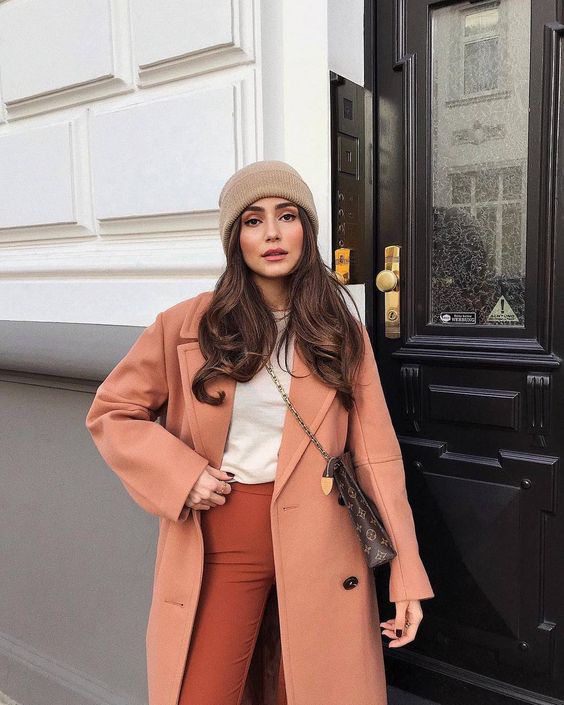 A winter look with a peachy coat, a white top, rust colored pants, a tan beanie and a printed bag is awesome