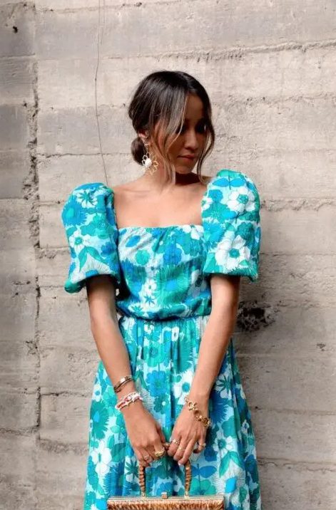 an elegant and bright floral wedding guest dress done in blue and gree, with a square neckline, puff sleeves and statement earrings for a summer wedding
