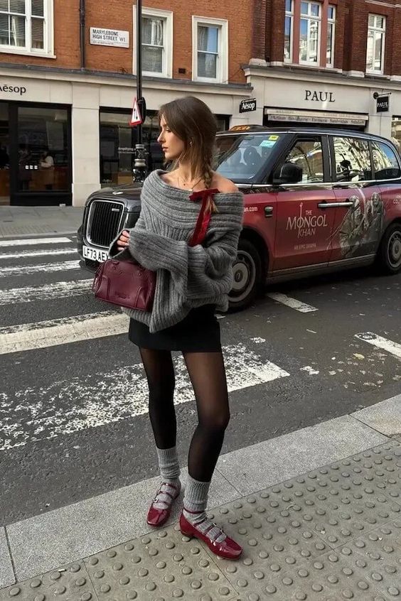 An eye catchy look with a grey off the shoulder sweater, a black mini, black tights, grey socks, red Mary Jane shoes and a burgundy bag