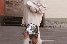 an oversized neutral sweater, a silver sequin fringe skirt, white cowboy boots and a neutral bag for a fashion statement
