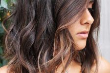 shoulder-length dark brown hair with copper highlights and messy waves is a relaxed and cool solution to try right now
