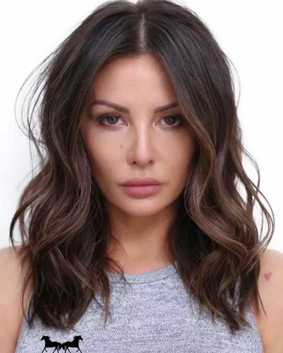 Stylish and chic dark brunette medium length layered hair with chestnut balayage and waves is wow