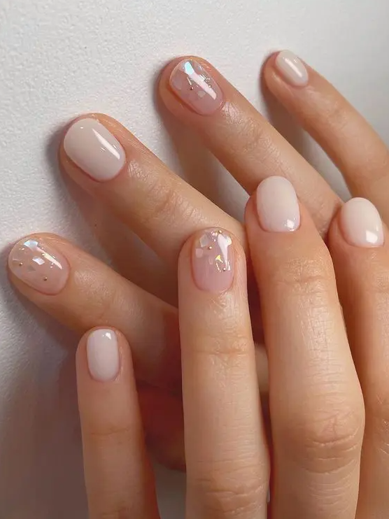 a neutral wedding manicure with milky and blush nails and gold polka dots and holographic touches on the nails